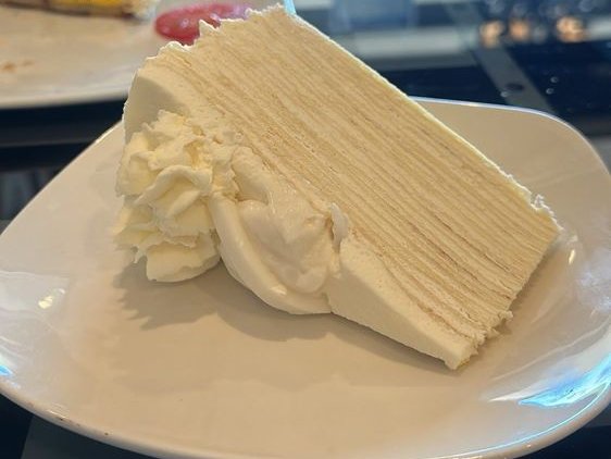 Slice of coconut crepe cake with dozens of thin layers and whipped cream on a white plate