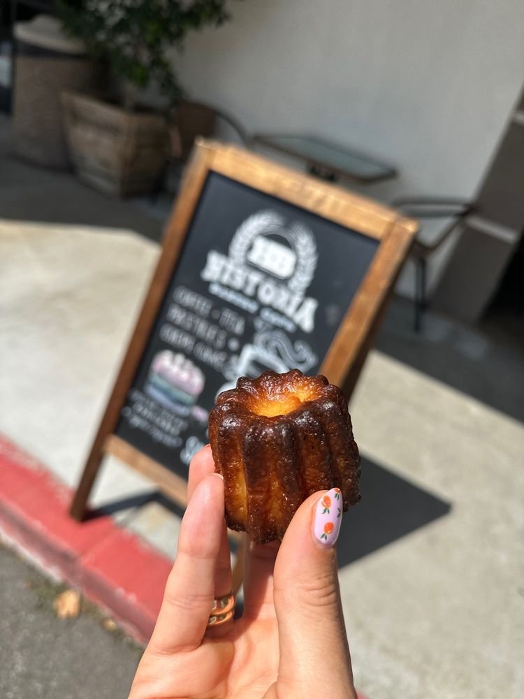 Canelé held in hand in front of the Historia chalkboard