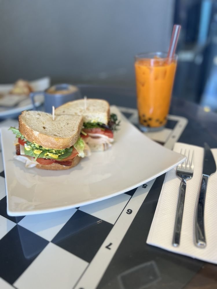 Sandwich halves on a square plate with an iced tea with boba